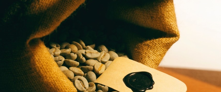 Green coffee beans spilling from a jute sack beside a blank sealed lot tag