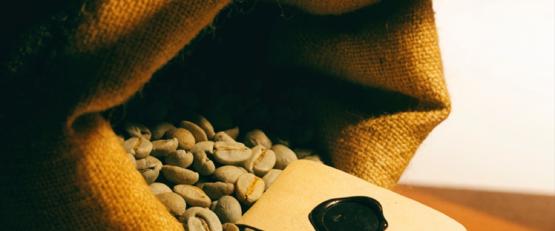 Green coffee beans spilling from a jute sack beside a blank sealed lot tag