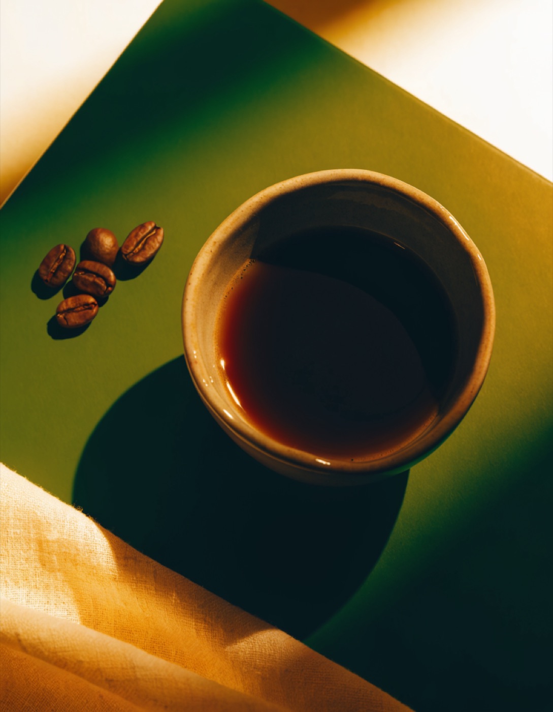 A cup of black coffee photographed from above beside roasted beans